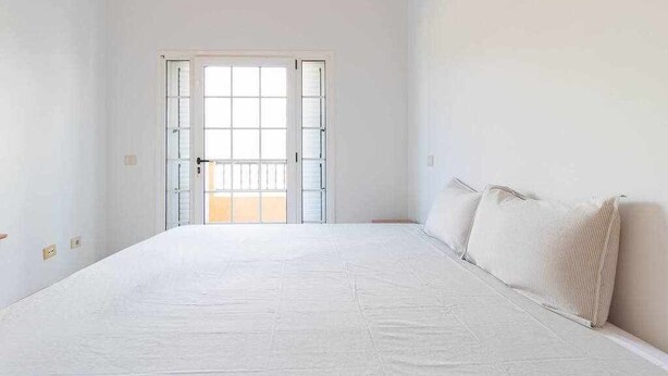 Ein Schlafzimmer mit einem großen Bett, einer Tür, die auf einen Balkon führt, und weißen Wänden.