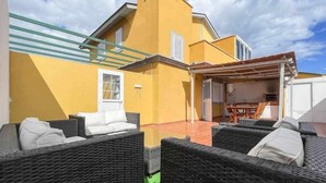 Ein gelbes Gebäude mit einer überdachten Terrasse, Korbmöbeln und einem Tisch.