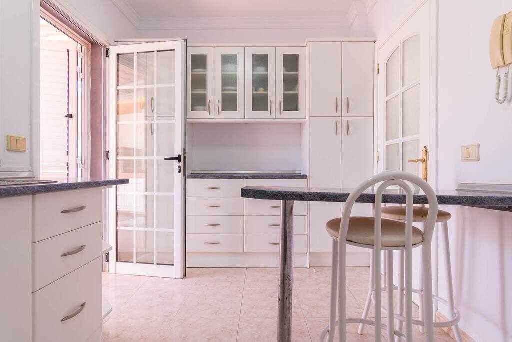 Une cuisine avec des meubles blancs, un plan de travail noir et une chaise blanche.