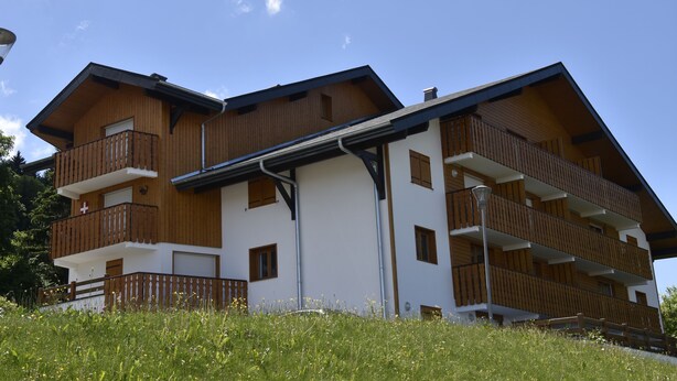 A multi-story wooden building with balconies, a white facade, and a clear blue sky.