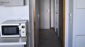 A narrow hallway with a microwave on a counter, wooden door frames, and a white refrigerator.