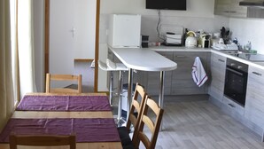 A modern kitchen with a dining area, featuring a white countertop, wooden chairs, and a TV mounted above the counter.