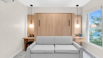 Una habitación moderna con sofá gris, armario de madera y escritorio con lámpara.