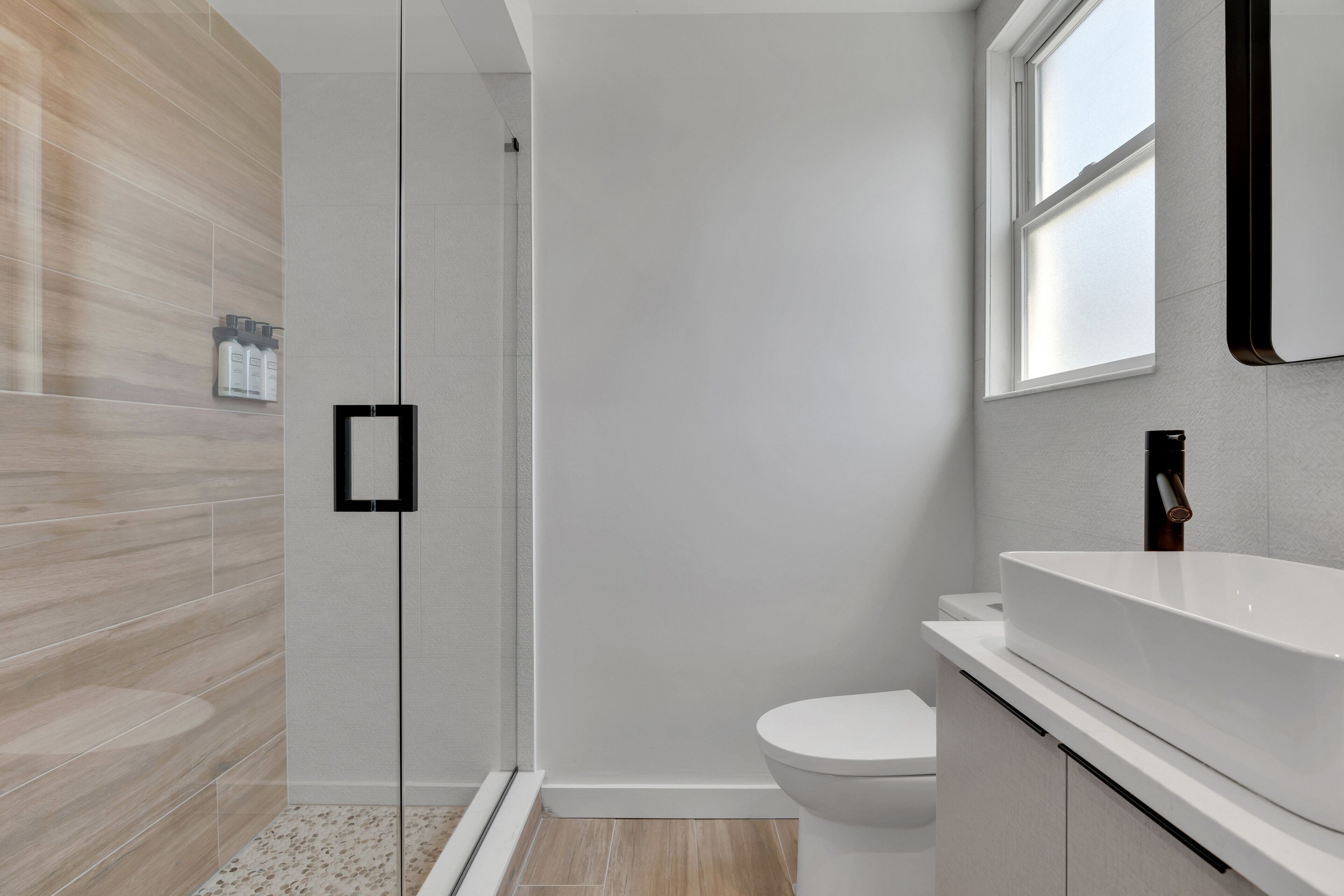 A modern bathroom with a glass shower enclosure, a white toilet, and a large sink with a mirror above it.