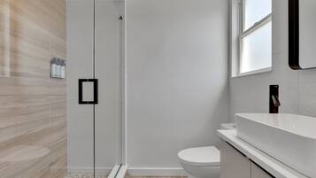 A modern bathroom with a glass shower enclosure, a white toilet, and a large sink with a mirror above it.