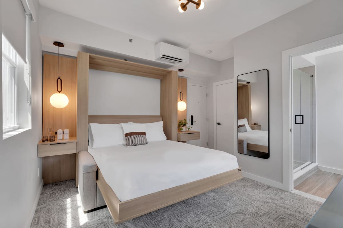 A modern bedroom with a wooden bed frame, a large mirror, and pendant lights.