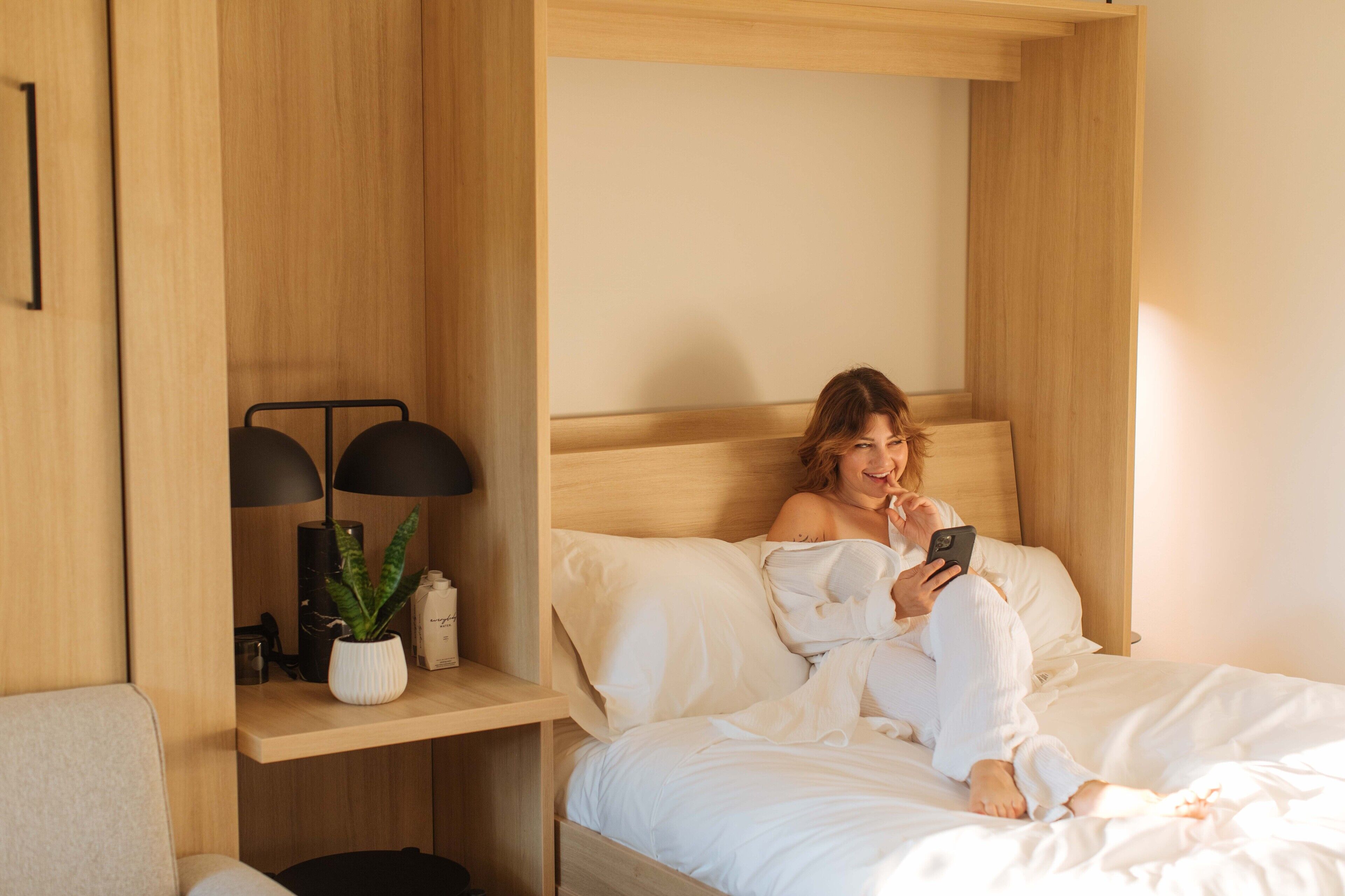 A bedroom with a bed, bedside table, lamp, and a potted plant.