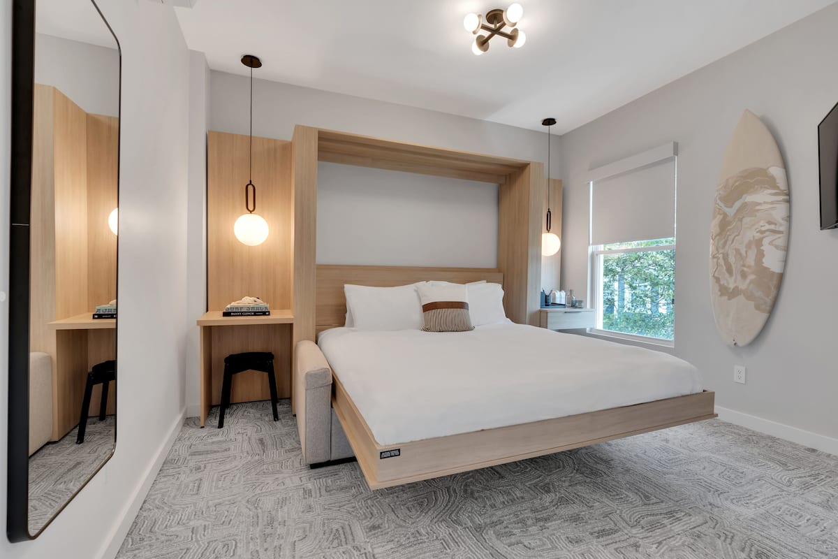 A modern bedroom with a floating bed, wooden accents, a desk, and a large window.