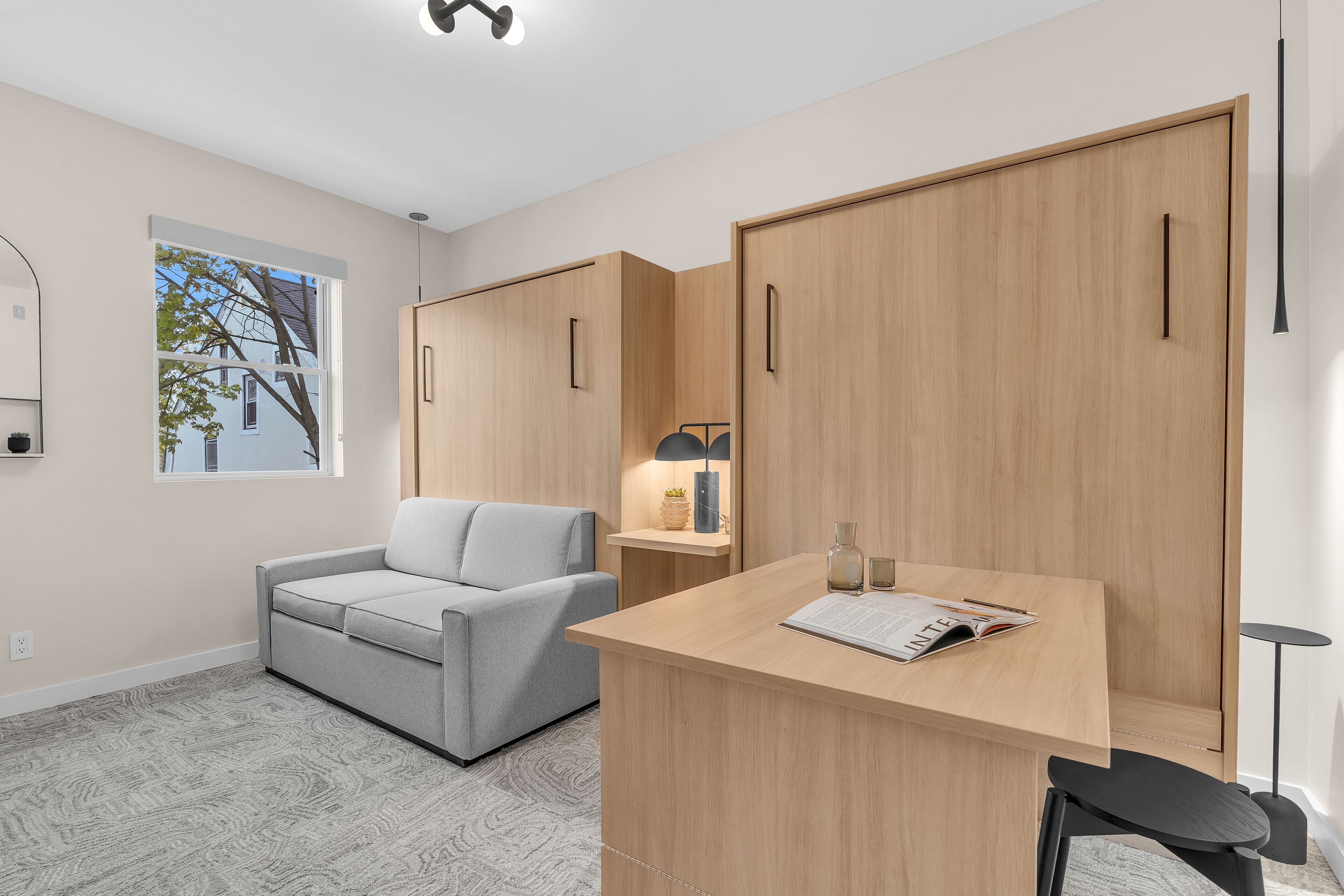 Ein modernes Zimmer mit einem grauen Sofa, einem Holztisch und einem Kleiderschrank.