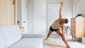 Una persona realizando una postura de yoga en una habitación con un sofá, un armario de madera y una puerta.