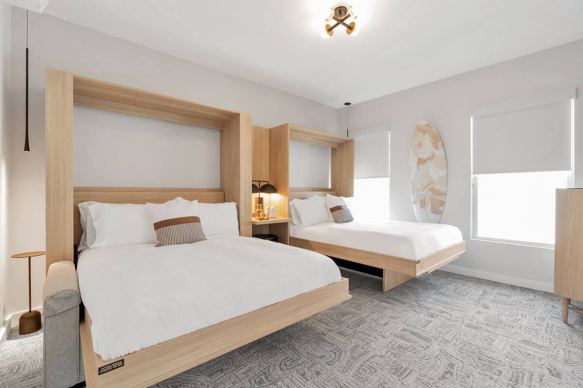 A modern hotel room with two beds, a large window, and a surfboard decoration.