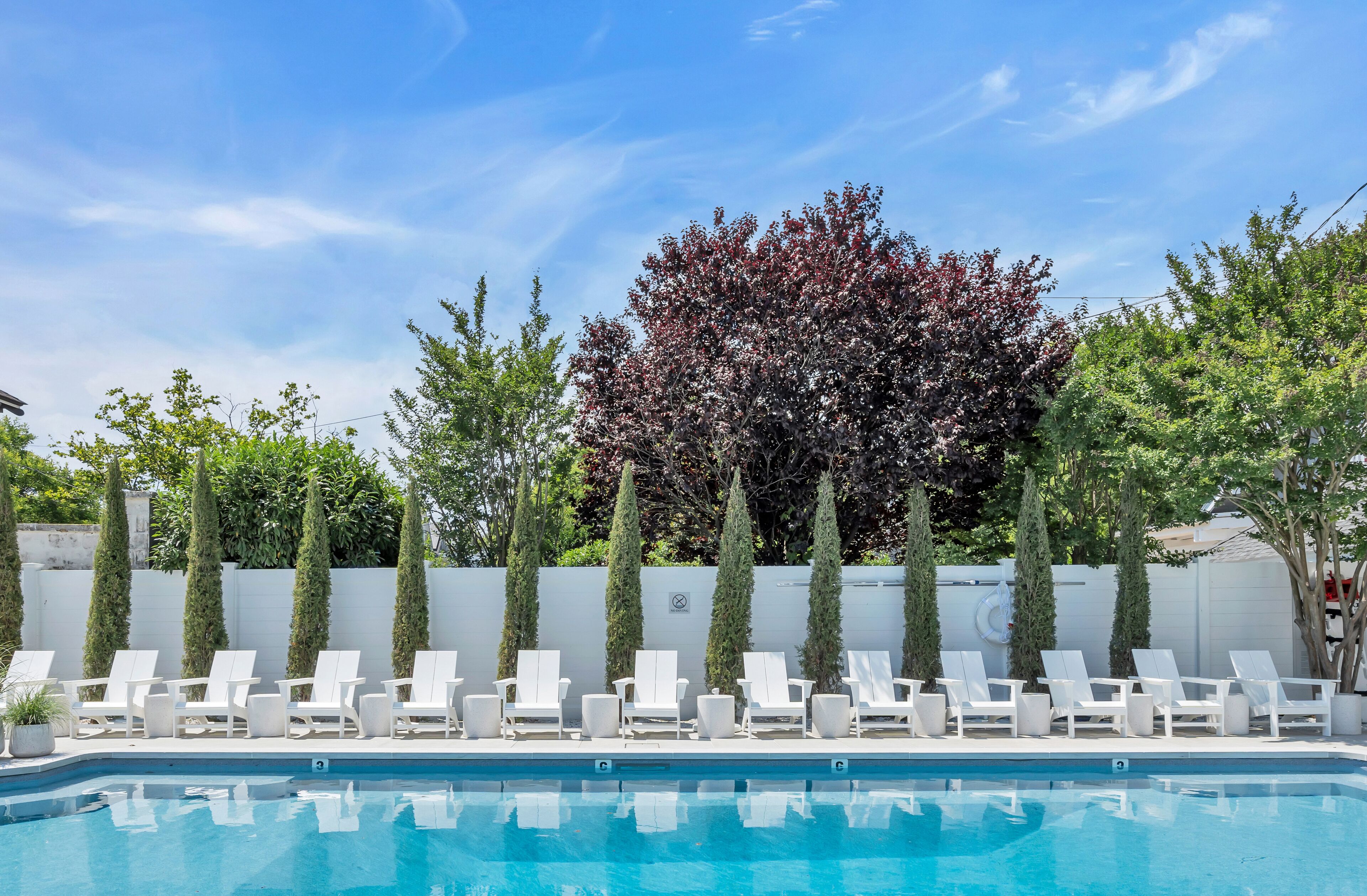 Ein Pool mit weißen Liegestühlen und ein Baum mit roten Blättern im Hintergrund.