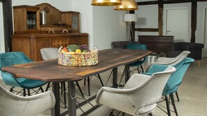 A dining area with a wooden table, teal and white chairs, a fruit basket, and a wooden cabinet. - Dream cottage (Menslage)