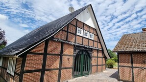 A traditional half-timbered building with a steeply pitched roof, a green door, and a satellite dish on the roof. - Dream cottage (Menslage)