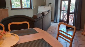A dining area with a wooden table and chairs, a sofa, and a window with curtains. - Ferienwohnung mit Fantastischem Ausblick, Direkt am Wald (Walkenried)