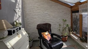 A sunlit patio with a black leather chair, a white dresser, and potted plants. - Ferienwohnung mit Fantastischem Ausblick, Direkt am Wald (Walkenried)