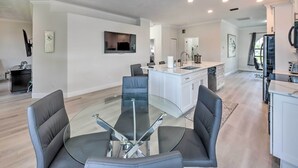 A modern kitchen with white cabinets, a central island, and a dining area with a glass table and black chairs. - Lanai + Pool: Dog-Friendly Home in Cape Coral! (Cape Coral)