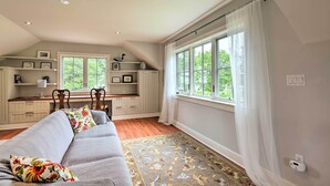 A spacious living room with a grey sofa, a patterned rug, and a large window with sheer curtains. - Barn-Like Studio Suite w/ Flowering Garden! (Titusville)