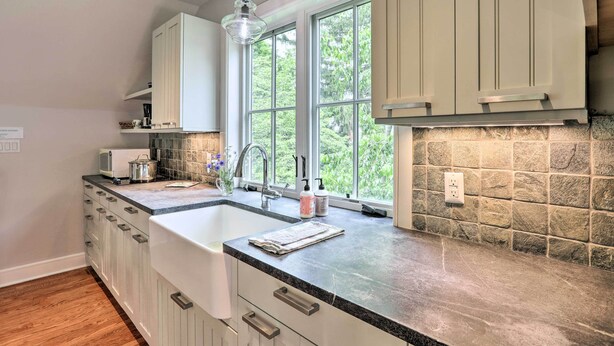 A kitchen with white cabinets, a granite countertop, a window with a view of greenery, and a hanging light fixture. - Barn-Like Studio Suite w/ Flowering Garden! (Titusville)