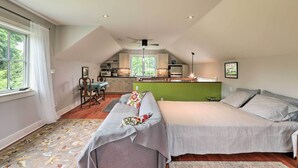 A loft bedroom with a large window, a kitchenette, and a green accent wall. - Barn-Like Studio Suite w/ Flowering Garden! (Titusville)
