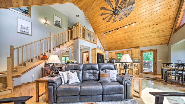 A spacious living area with a leather sofa, wooden flooring, a large wooden ceiling, and a staircase leading to an upper level. - Spacious Murphy Chalet w/ Hot Tub: Mtn Views! (Murphy)