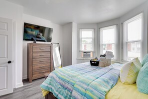 Een slaapkamer met een bed, een kaptafel, een televisie, ramen en een kleine tafel.