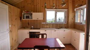 Een kleine keuken met houten wanden, een rode tafel en een raam met uitzicht op een tuin.