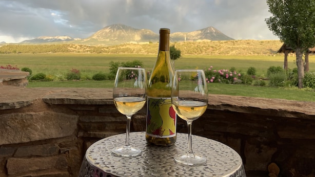 Une table avec une bouteille de vin et deux verres, placée sur un mur de pierre donnant sur un paysage montagneux.