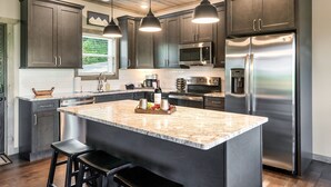 Une cuisine moderne avec des meubles de couleur sombre, des appareils en acier inoxydable et un grand îlot central doté de tabourets de bar.