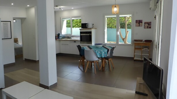 A modern kitchen with white cabinets, a dining area with a table and chairs, and a TV on a stand. - Large air-conditioned T2, private parking near the center and beach (Banyuls-sur-Mer)