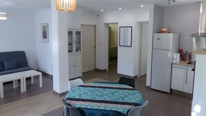 A compact living space with a dining table, chairs, a sofa, a kitchen area with a refrigerator, and a hallway leading to another room. - Large air-conditioned T2, private parking near the center and beach (Banyuls-sur-Mer)