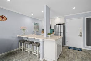 A modern kitchen with a central island, bar stools, a refrigerator, and a door with a keypad lock.