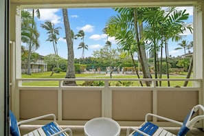 A room with a view of a tropical garden, two white chairs with blue cushions, and a small table.