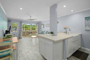 A modern kitchen with a central island, a dining area with a table and chairs, and a view through the glass doors.