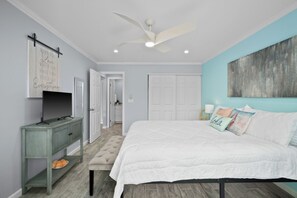 Une chambre à coucher comprenant un lit, une commode, un ventilateur de plafond et une porte donnant sur une autre pièce.
