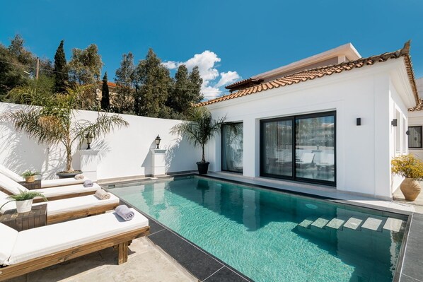 Una casa moderna con piscina, paredes exteriores blancas y techo de tejas.