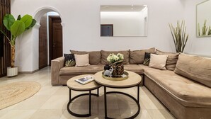Un salon moderne avec un canapé d’angle beige, deux petites tables rondes et un grand miroir mural.