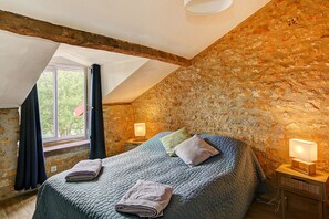 Ein Schlafzimmer mit Steinwand, einem Bett mit Steppdecke, zwei Nachttischlampen und einem Fenster mit Vorhängen.