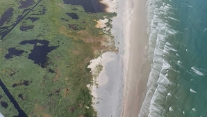 Ett flygbildsbild av ett kustområde med en strand, grön våtmark och en klar himmel.