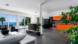 Un salón moderno con televisor grande, asientos cómodos y vista al mar.