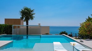 Una piscina con vista al mar, una palmera y un edificio moderno.