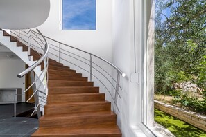 A modern staircase with wooden steps and a metal railing, leading to a room with a stone fireplace.