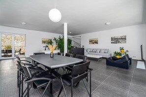 A modern dining area with a large table and chairs, a sofa, and a staircase leading to an upper level.