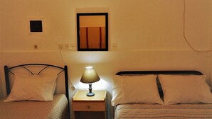 Een kleine, eenvoudige kamer met twee eenpersoonsbedden, een nachtkastje met een lamp, een spiegel en een klein raam.
