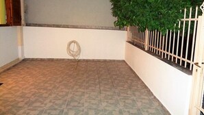 Een klein, afgesloten terras met betegelde vloer, een plant in pot en een witte omheining.