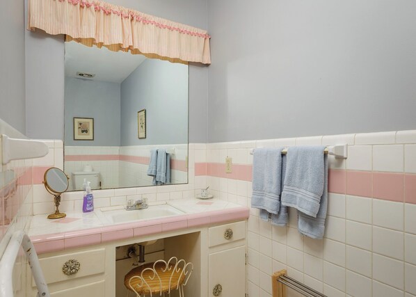 A bathroom with a white sink, a mirror, a vanity with drawers, a chair, and towels hanging on a rack. - Bettie’s Lake Cottage on Wilson Lake. (Muscle Shoals)
