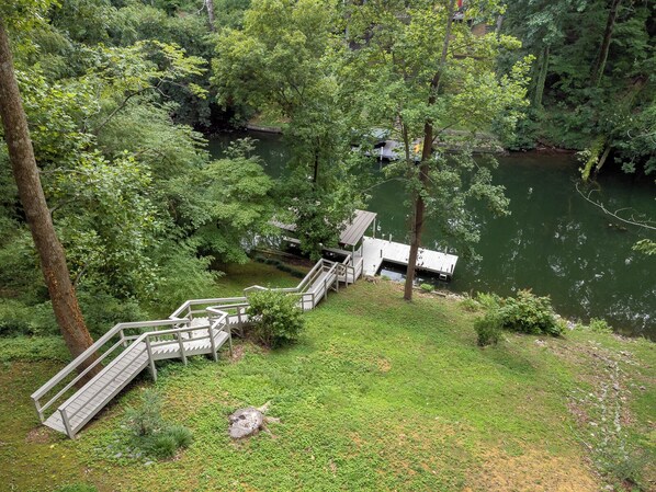 A wooden dock with steps leading into a lake surrounded by dense greenery.