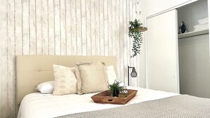 Una cama bien tendida con cabecera, una mesita de noche con una planta y una lámpara colgante.