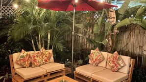 Un espacio al aire libre con dos sofás y una mesa de centro, rodeado de plantas y luces colgantes.