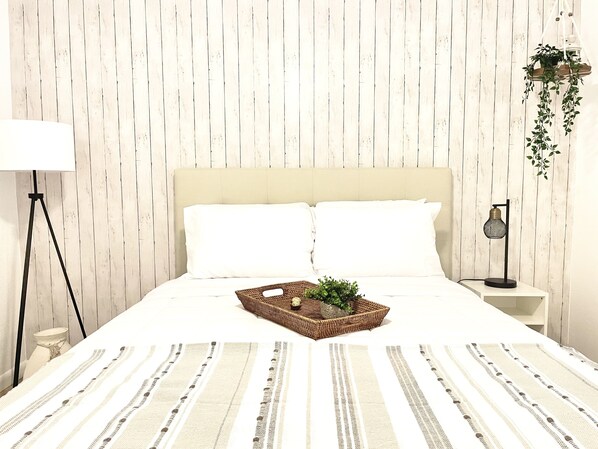 A neatly made bed with white linens, a woven basket with greenery, and a hanging plant. - Bon Voyage - Cozy 2 - bedroom residential home (Naples)